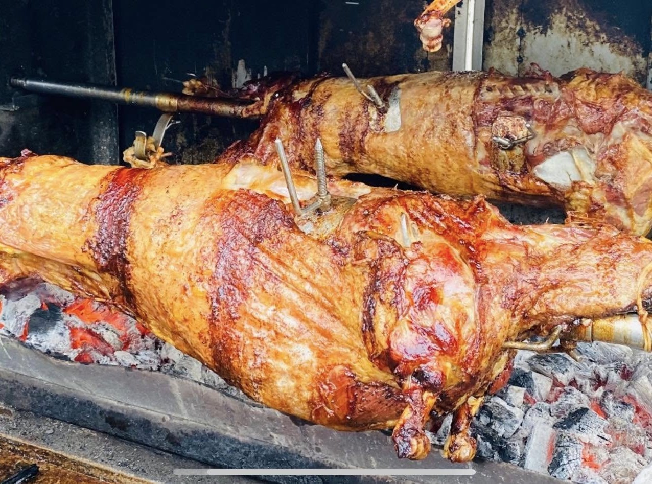 Whole lambs roasting on a spit over glowing coals — traditional Bosnian-style preparation