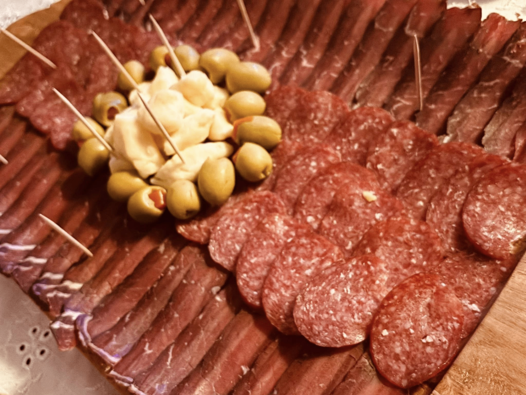 Charcuterie platter of sliced cured beef, salami and sudžuk with green olives and creamy dip in the center