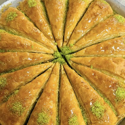 Round tray of pistachio-dusted baklava cut into wedges