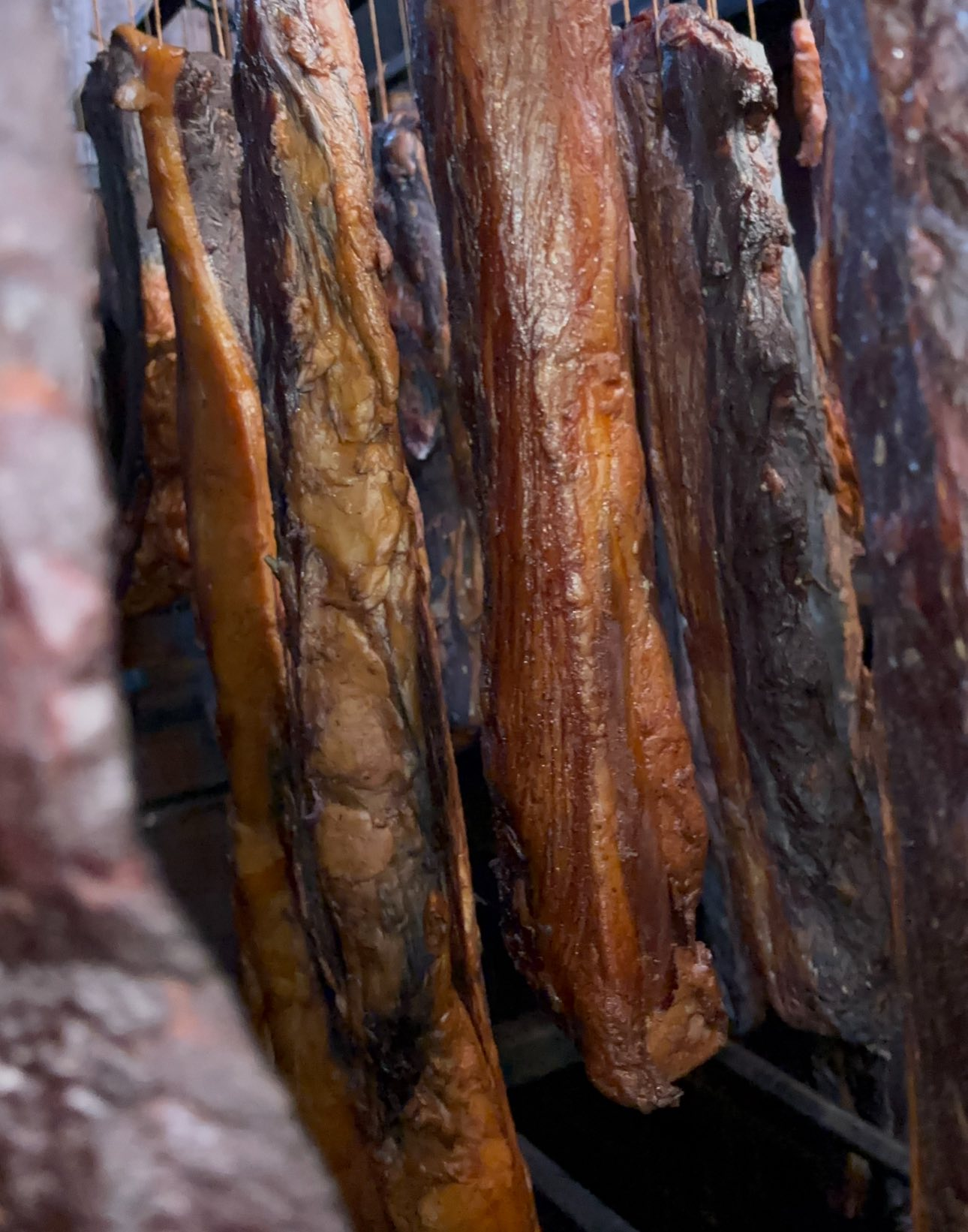 Whole pršuta and cured beef hanging in the smokehouse