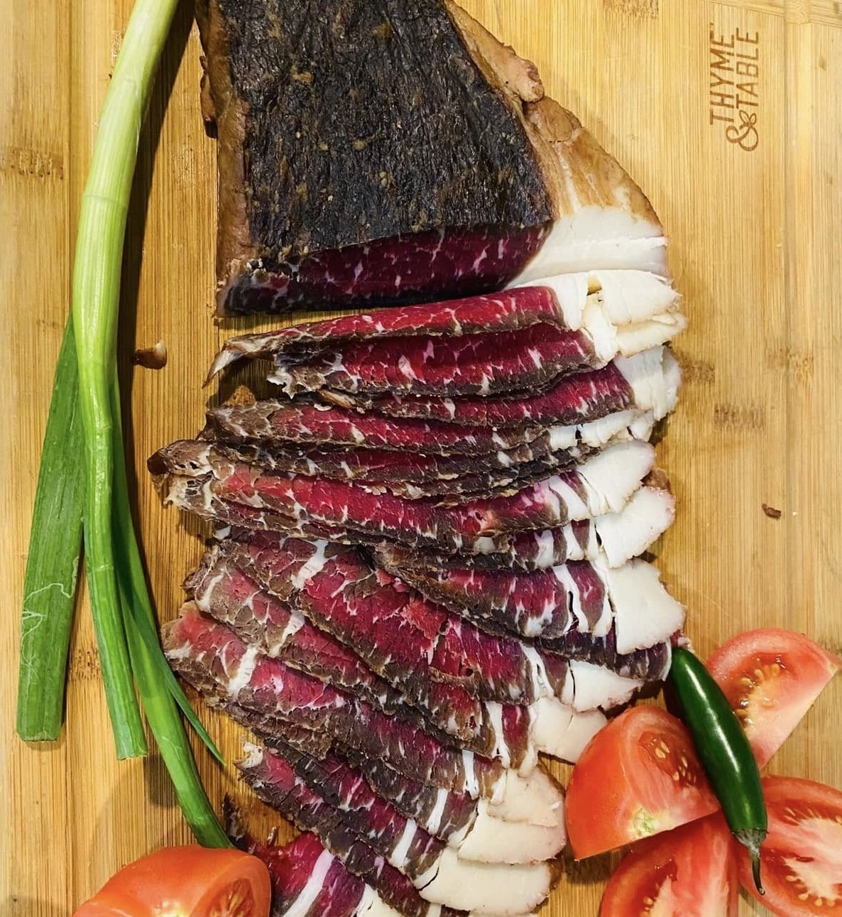 Whole and sliced suho meso on a wooden board with scallion and tomato